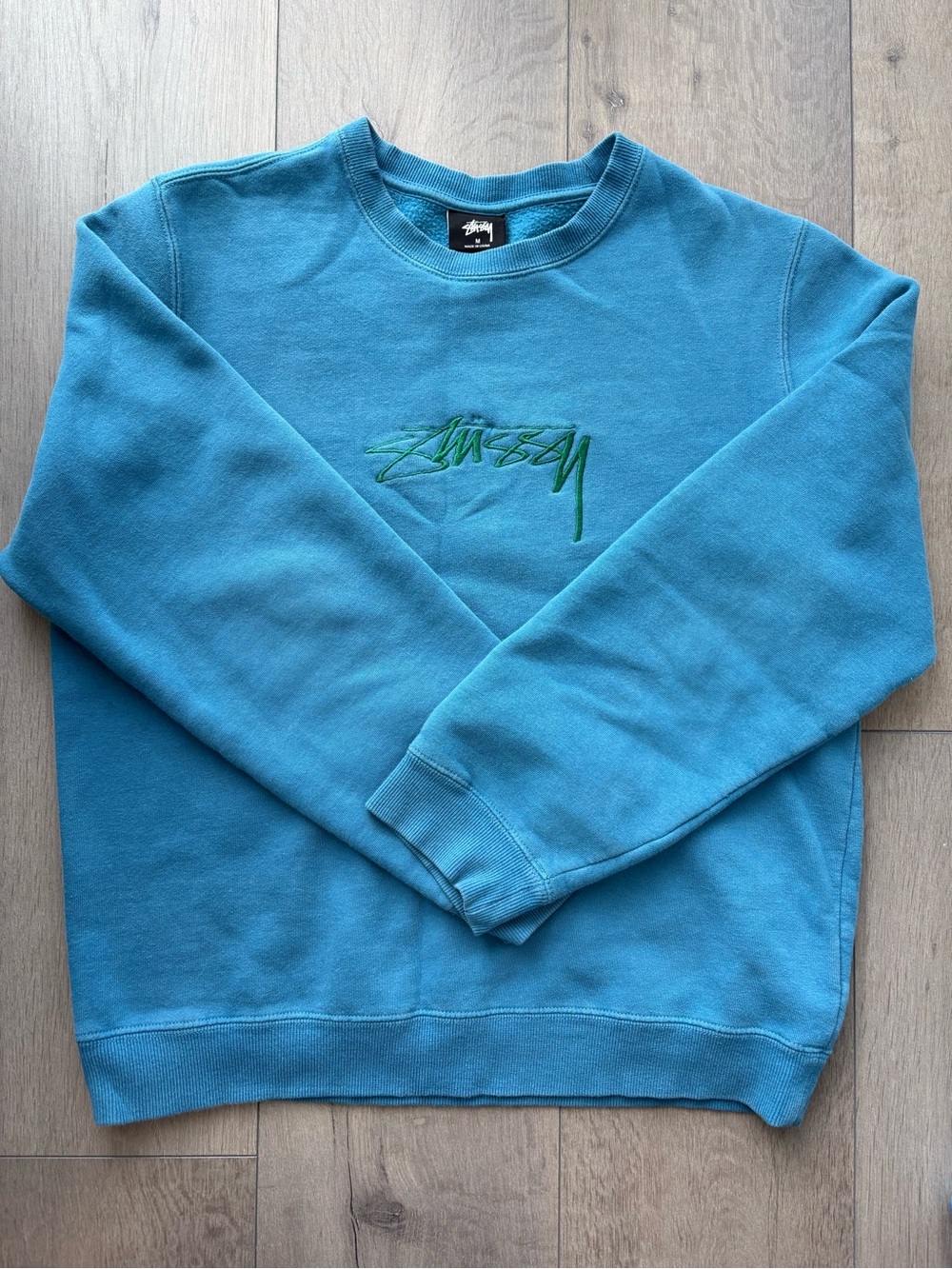 Stüssy crew-neck sweatshirt featuring a green embroidered logo on the chest
